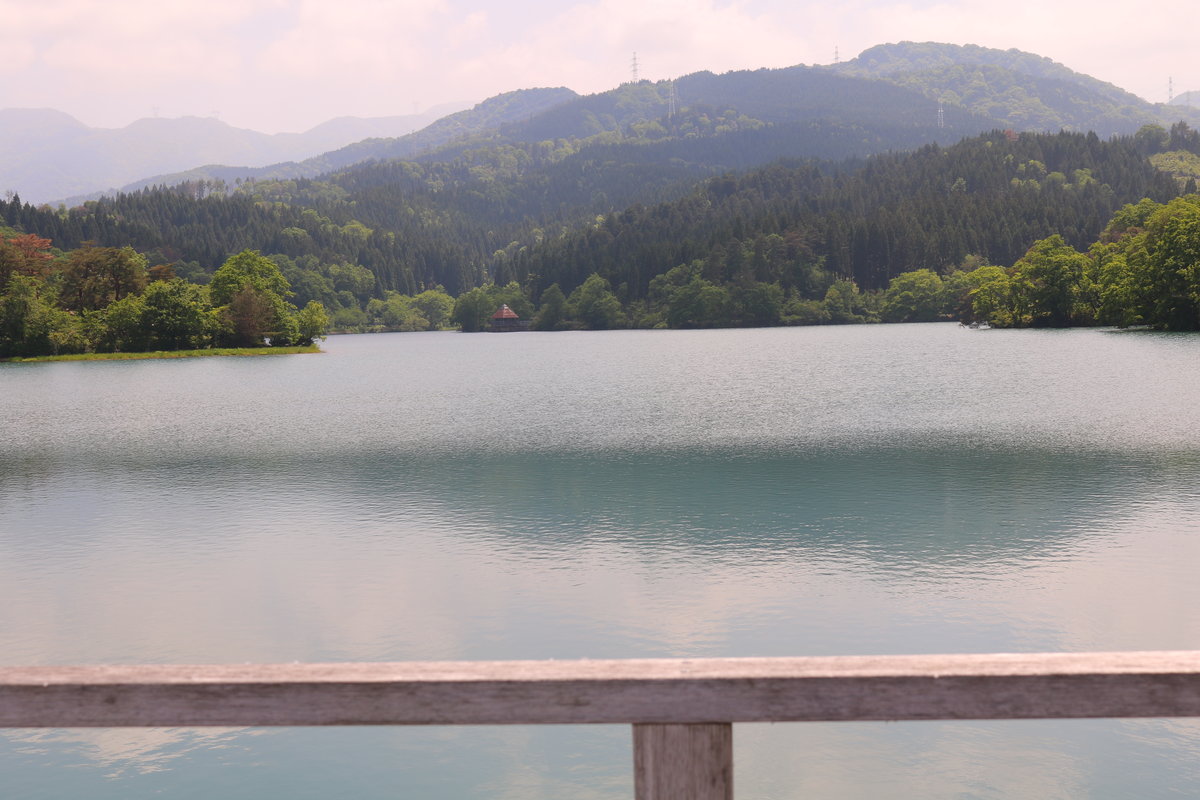 エメラルドグリーンの水面が広がる美しい桜ヶ池と背後に連なる里山の風景